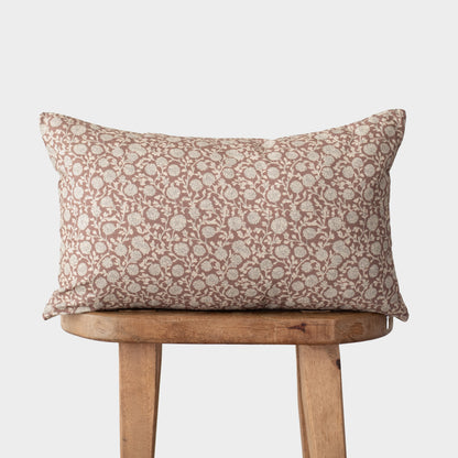Rectangular throw pillow with rust and cream floral damask pattern resting on wooden chair.