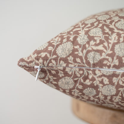 Rectangular pillow with brown and cream damask pattern, white zipper closure, and light wooden base visible.