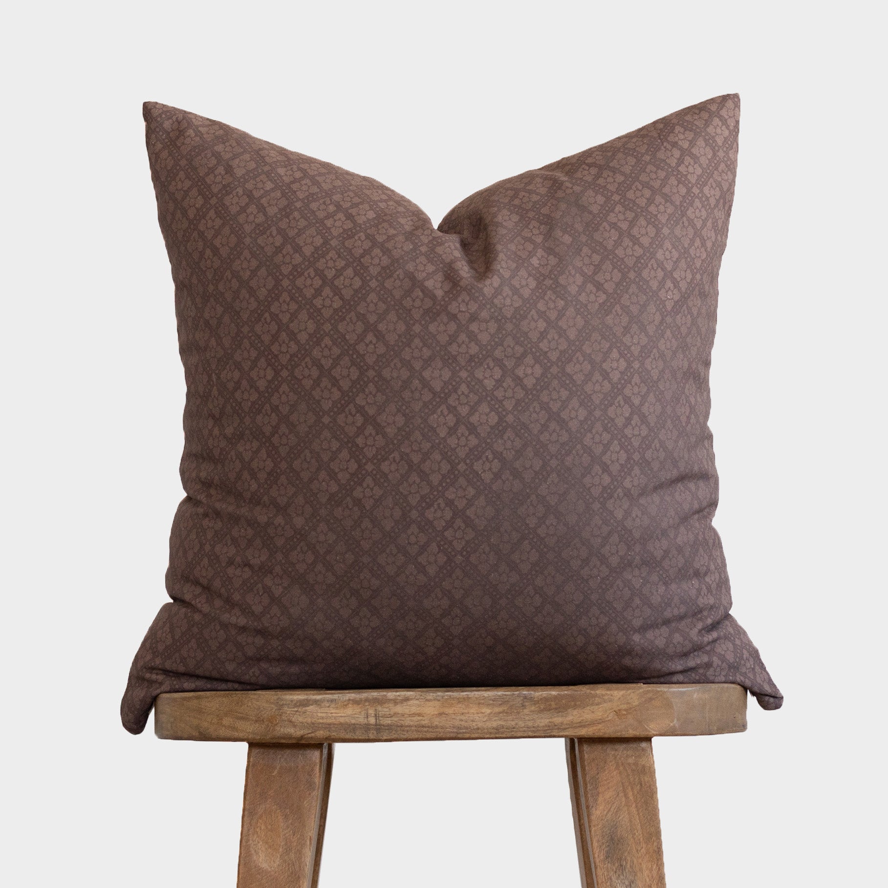 Maroon quilted pillow with diamond pattern displayed on wooden stool.