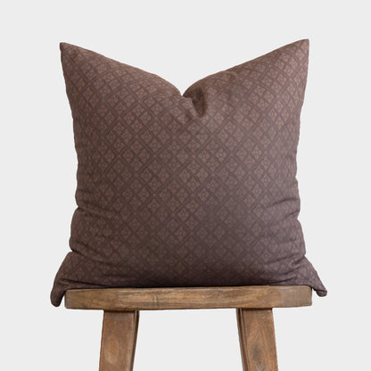 Maroon quilted pillow with diamond pattern displayed on wooden stool.