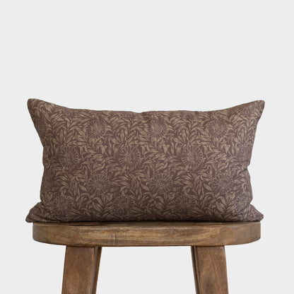 Brown rectangular lumbar pillow with allover leaf and floral damask pattern, displayed on wooden stool.