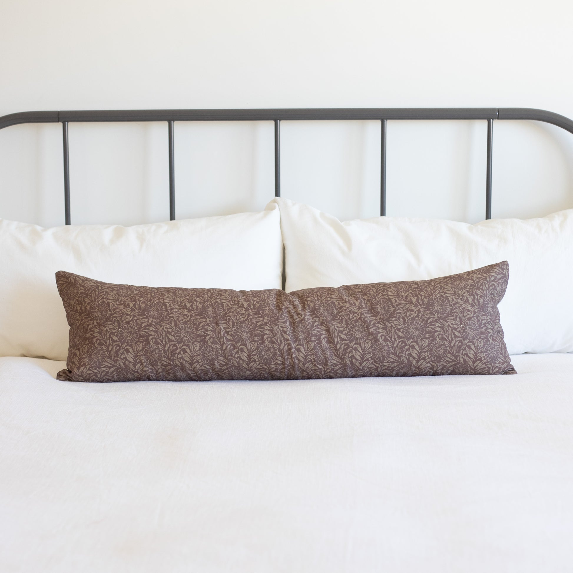 Brown damask patterned lumbar pillow on bed with white pillows and metal headboard.