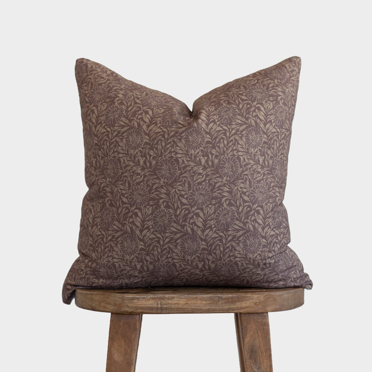 Brown damask patterned pillow with envelope back displayed on wooden stool.