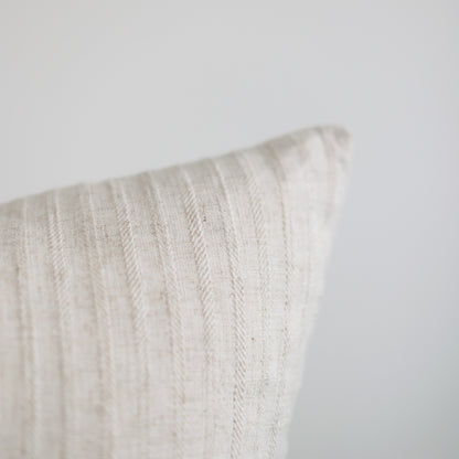 Cream-colored textured pillow with vertical woven pattern and piped edge detail.