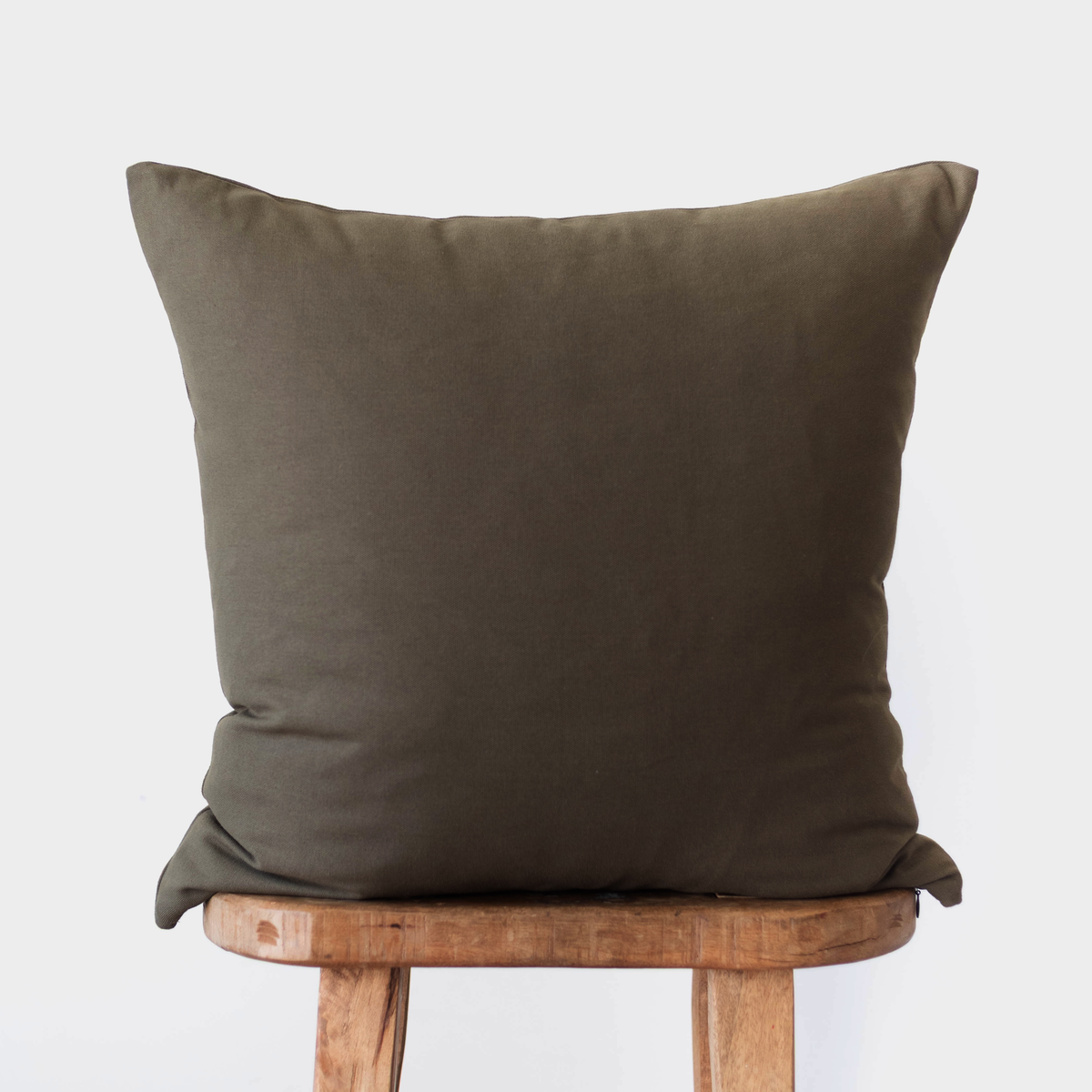 Dark olive square pillow with solid linen texture resting on wooden chair.