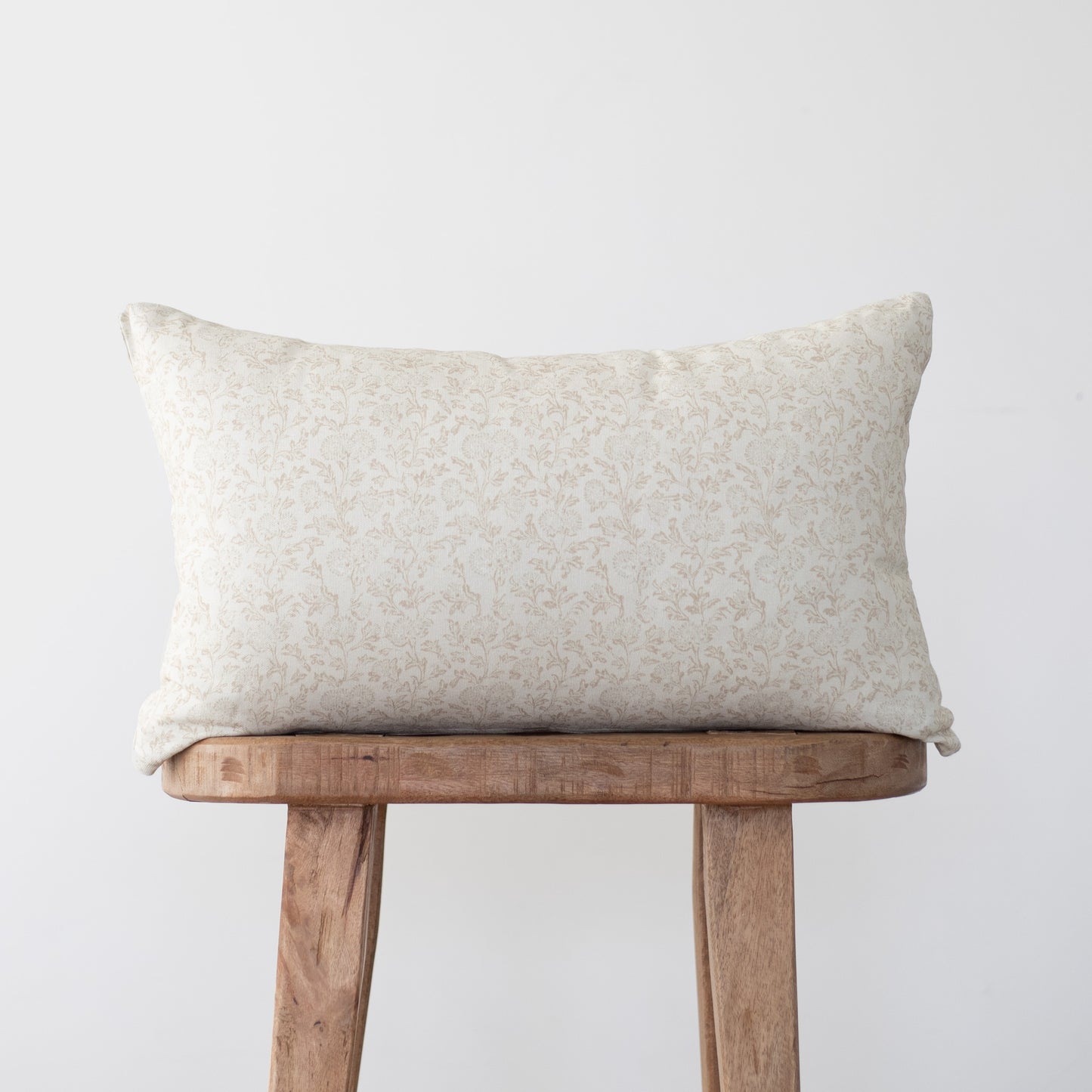 Cream rectangular pillow with subtle leaf pattern resting on wooden stool.