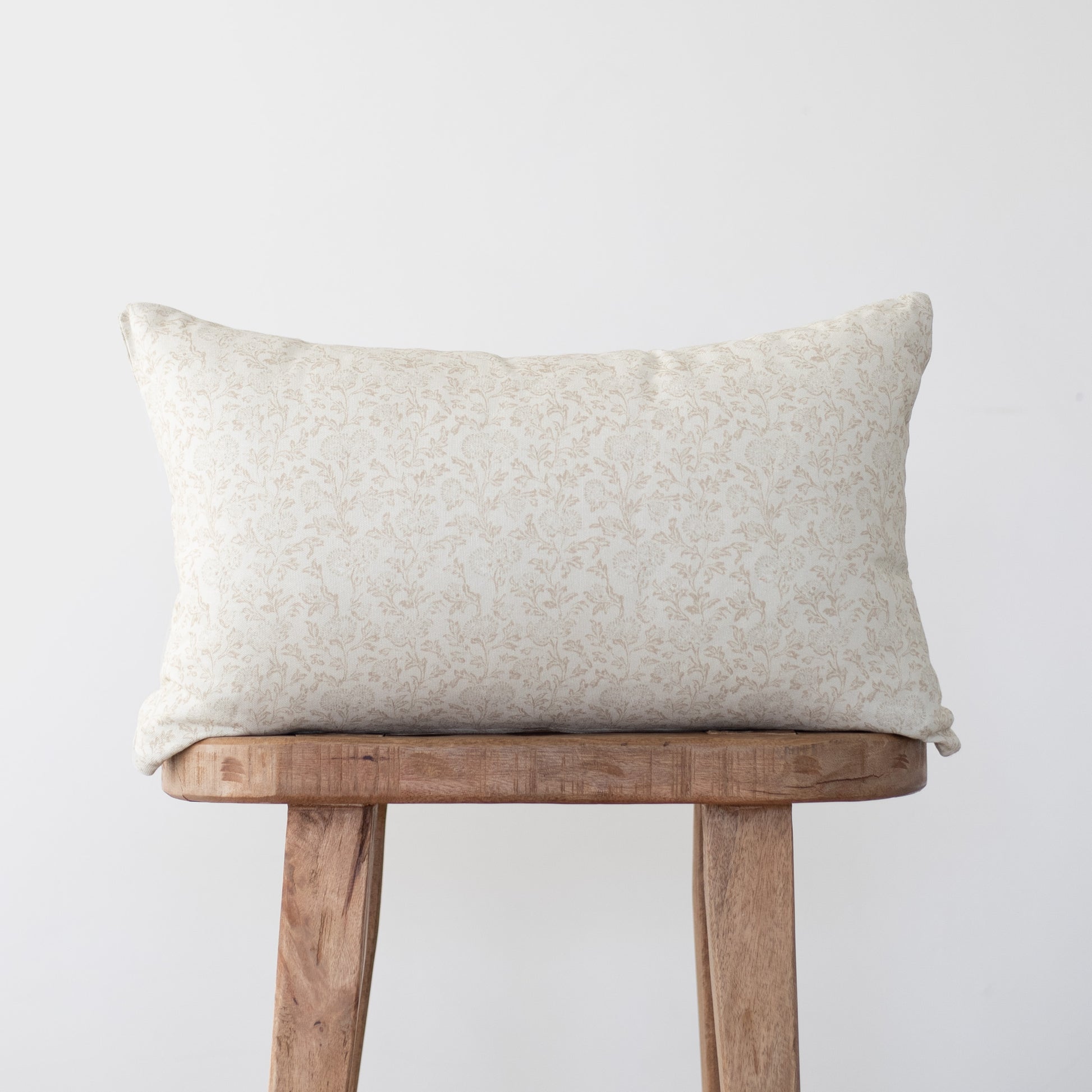 Cream rectangular pillow with subtle leaf pattern resting on wooden stool.