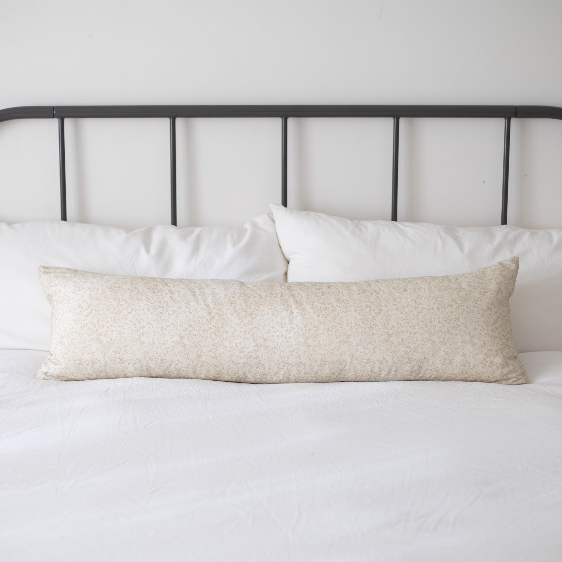 Cream textured lumbar pillow displayed on a bed with white pillows and black metal headboard.