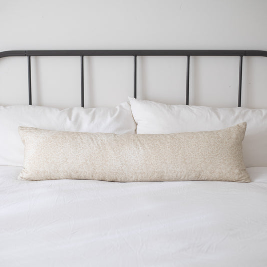 Cream textured lumbar pillow displayed on a bed with white pillows and black metal headboard.