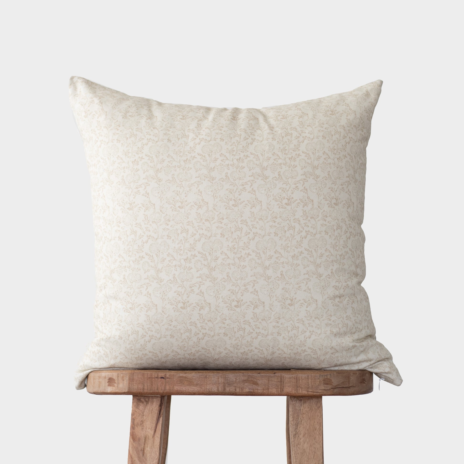 Cream-colored decorative pillow with subtle damask pattern resting on wooden stool.