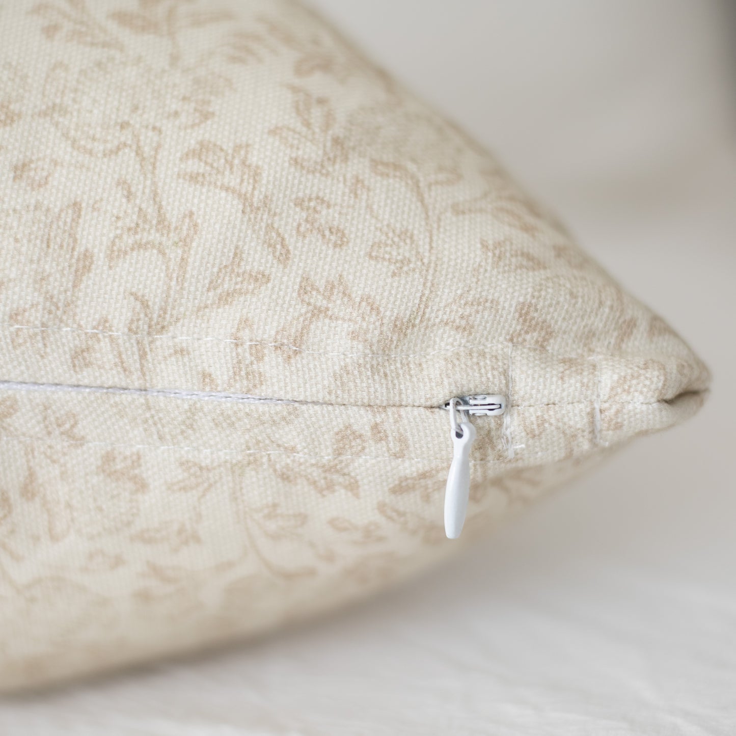 Beige decorative pillow with damask pattern and white zipper closure.