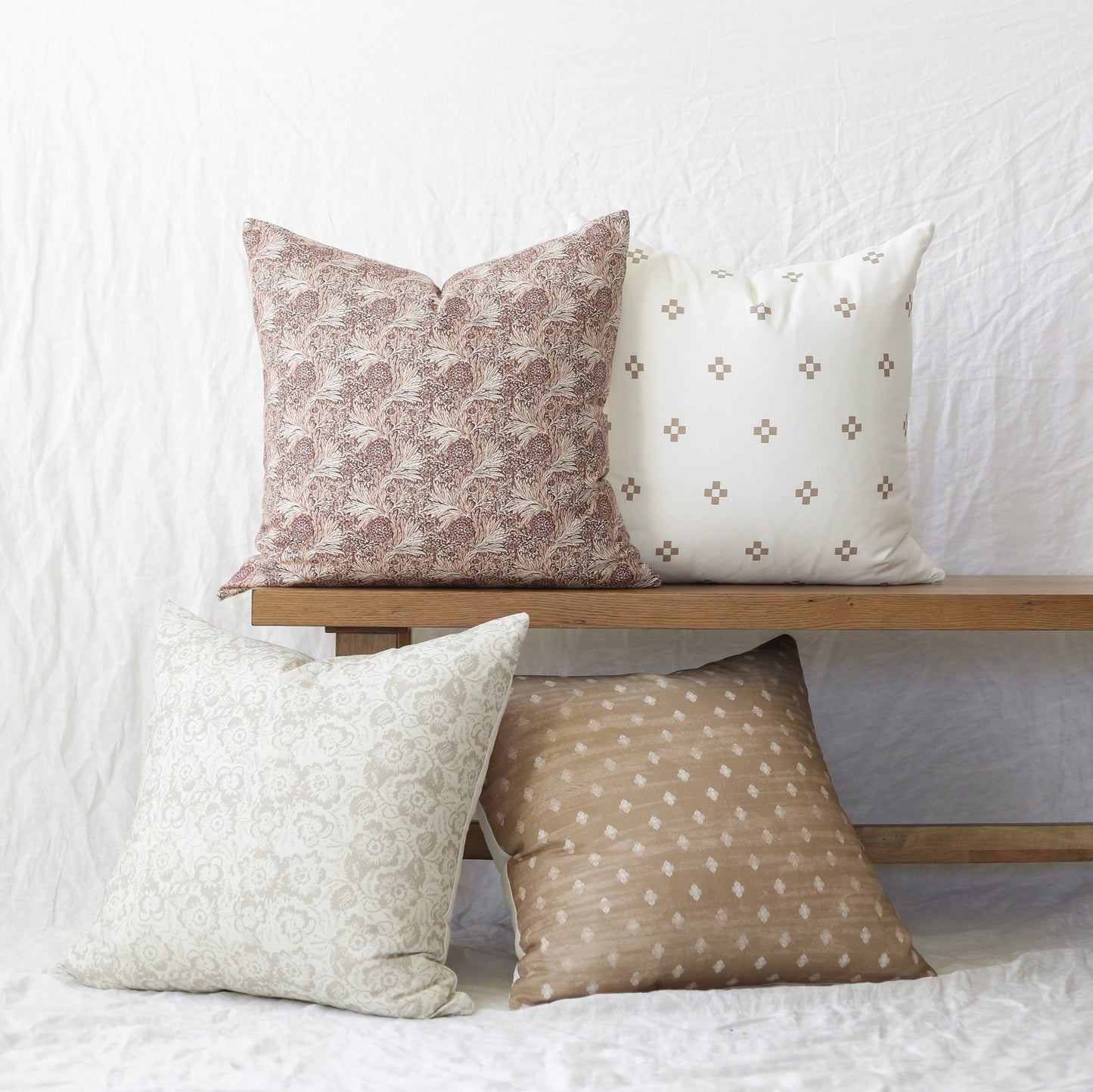 Four decorative pillows in varying patterns: mauve damask, cream with gray crosses, cream with ornamental design, and tan wit