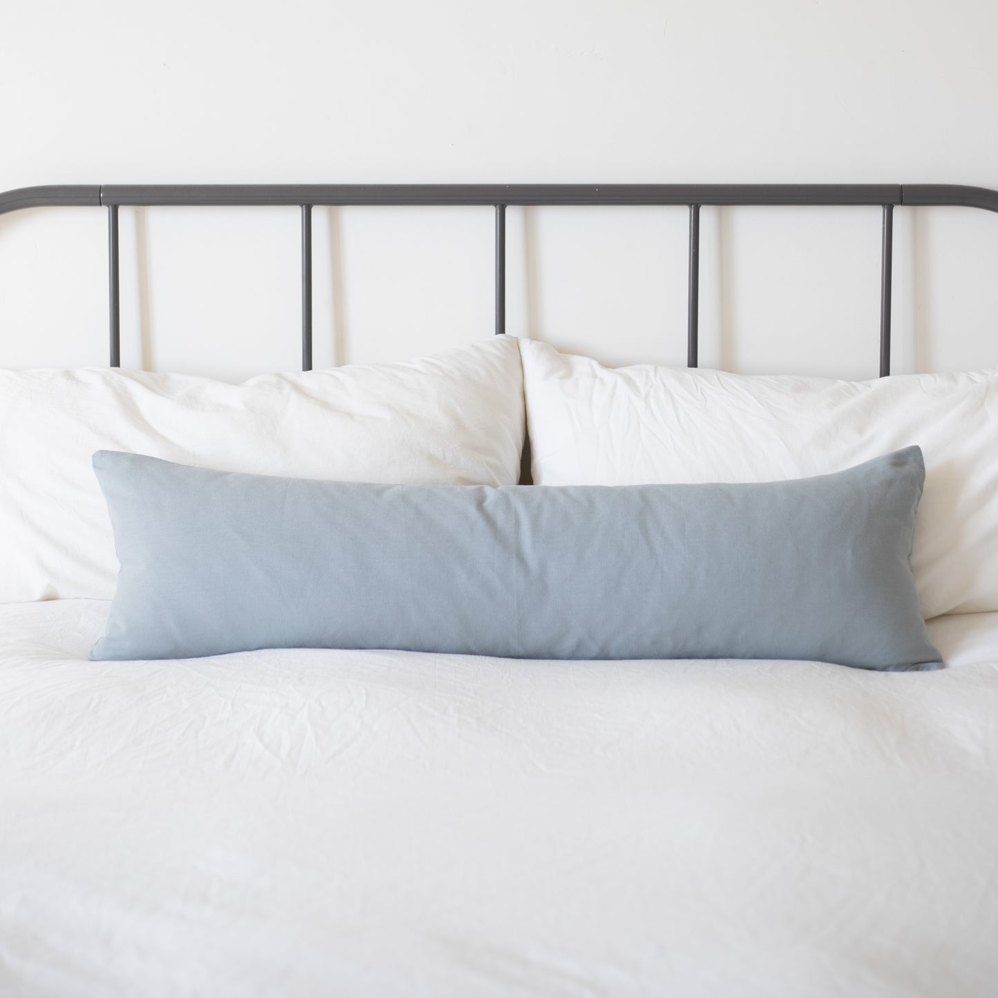 Dusty blue rectangular pillow displayed on a bed with white bedding and metal headboard.