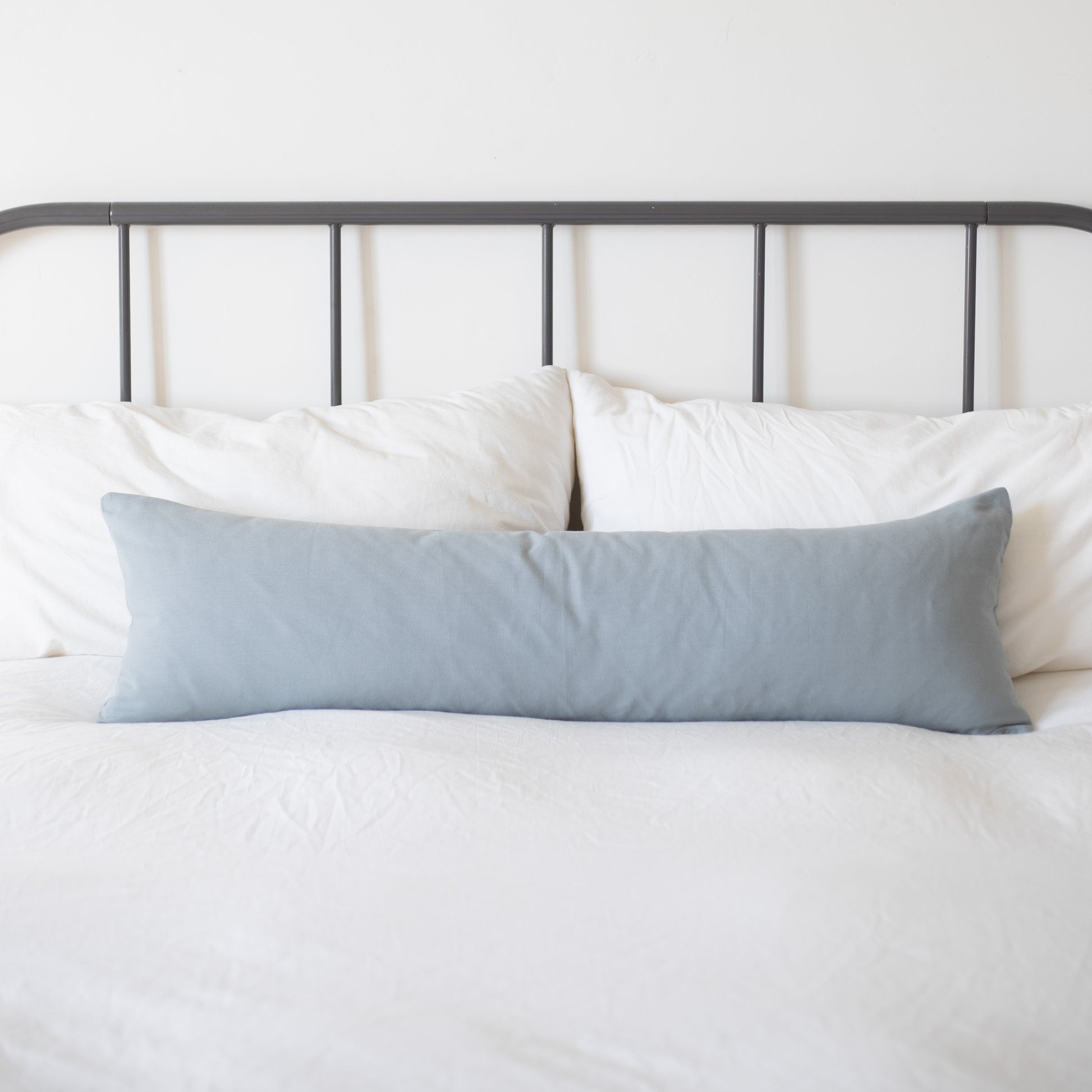 Dusty blue rectangular pillow displayed on a bed with white bedding and metal headboard.