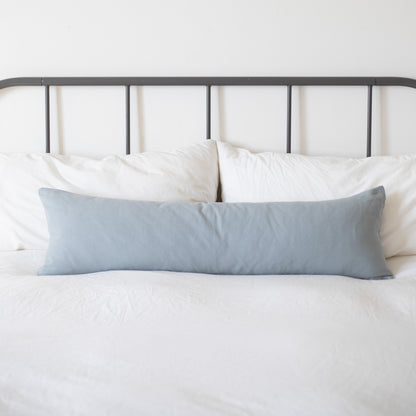 Dusty blue rectangular pillow displayed on a bed with white bedding and metal headboard.
