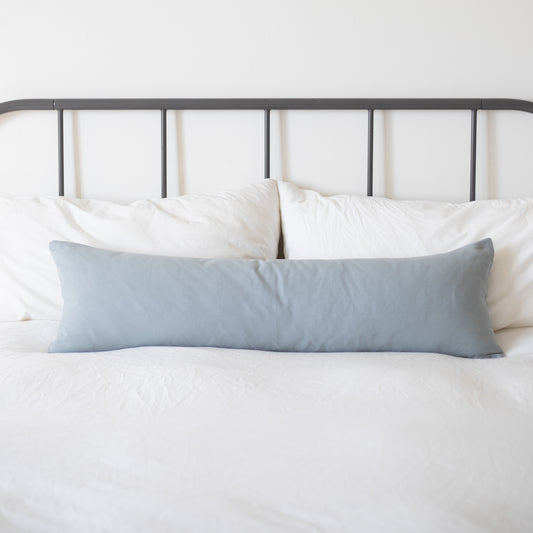 Dusty blue rectangular pillow displayed on a bed with white bedding and metal headboard.