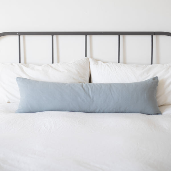 Dusty blue rectangular pillow displayed on a bed with white bedding and metal headboard.