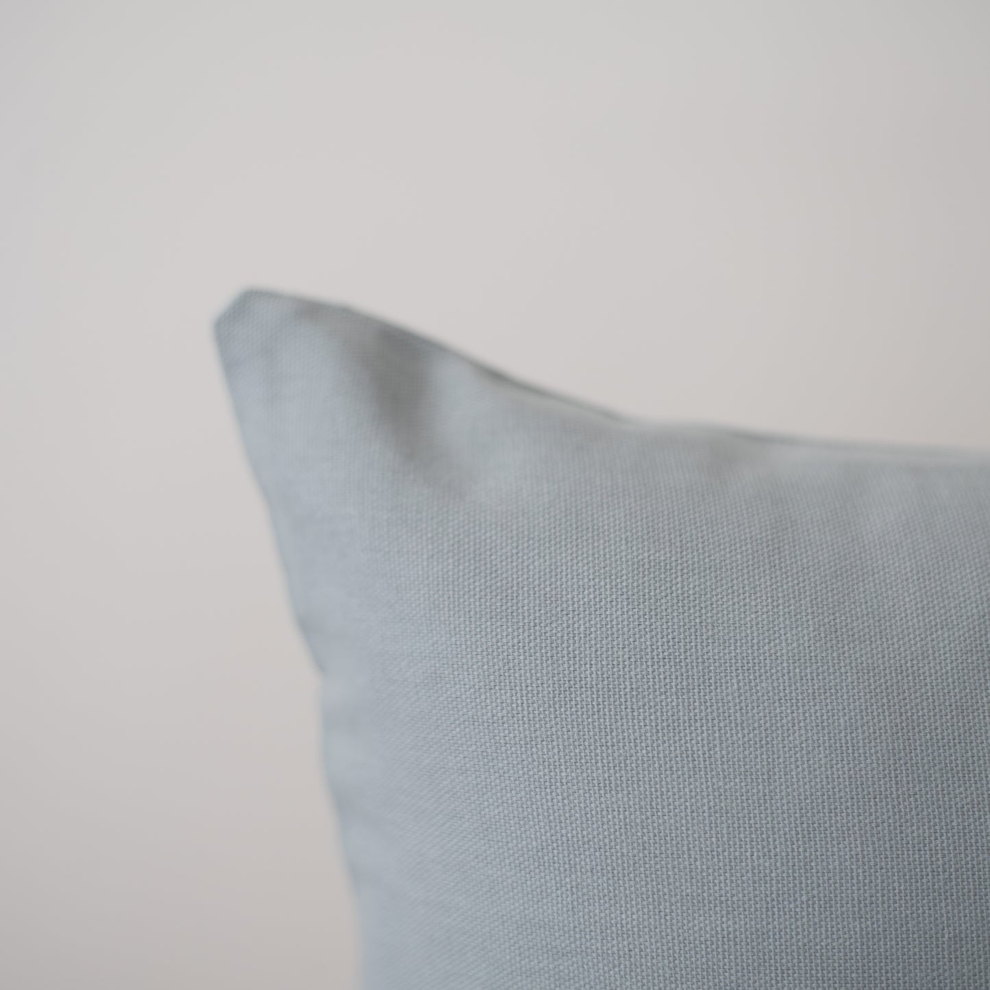 Dusty blue pillow with textured fabric weave and soft, rounded corner edge.
