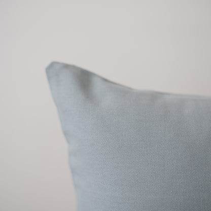Dusty blue pillow with textured fabric weave and soft, rounded corner edge.