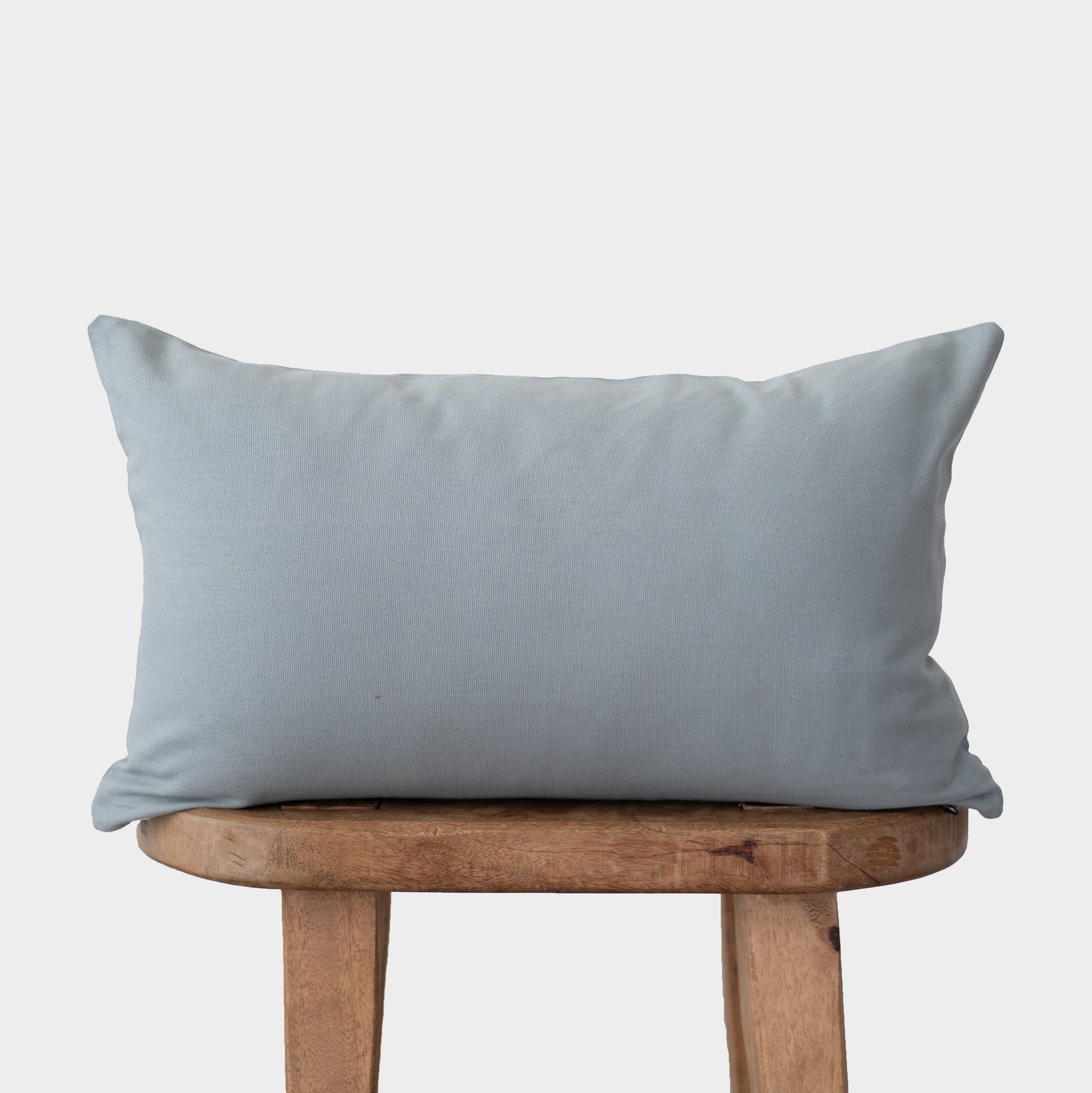 Dusty blue rectangular pillow with flange edges resting on a wooden bench.