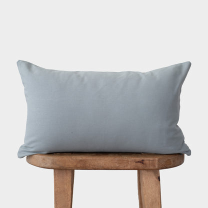 Dusty blue rectangular pillow with flange edges resting on a wooden bench.