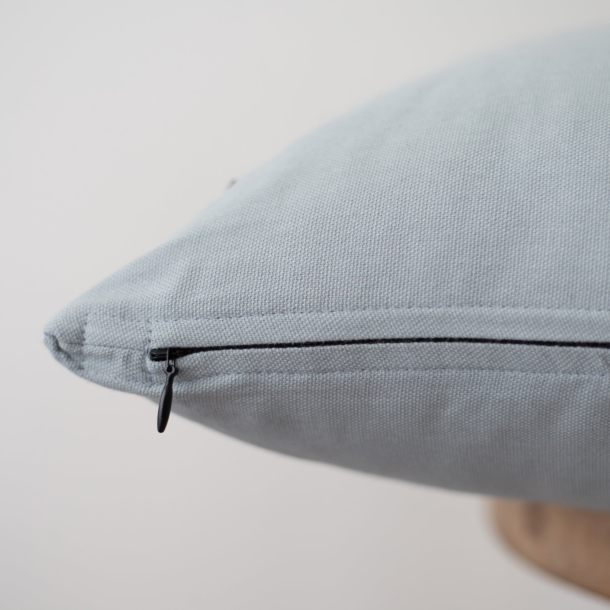 Dusty blue pillow cover with black zipper closure detail visible on seam.