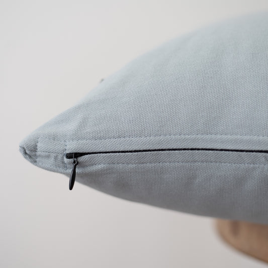Dusty blue pillow cover with black zipper closure detail visible on seam.