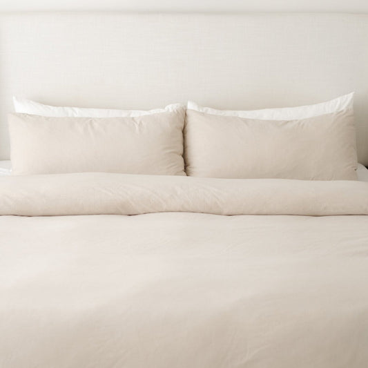 Beige duvet cover set with two pillows and insert on a bed against a white headboard.