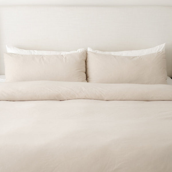 Beige duvet cover set with two pillows and insert on a bed against a white headboard.