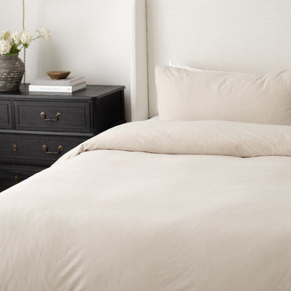 Beige duvet cover and pillowcases on a bed next to a black nightstand with white flowers and books.