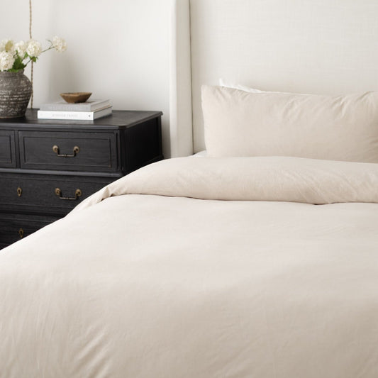 Beige duvet cover and pillowcases on a bed next to a black nightstand with white flowers and books.