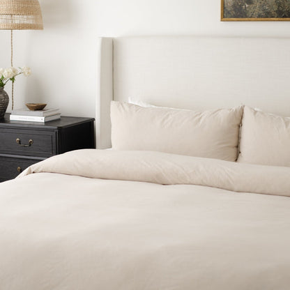Beige duvet cover set on a king bed with matching pillowcases and upholstered headboard.