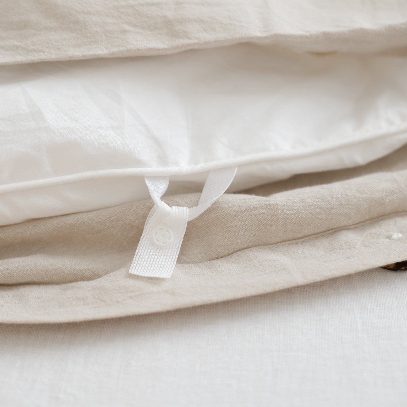 Beige and cream folded duvet cover with white button closure tab visible on layered fabric.