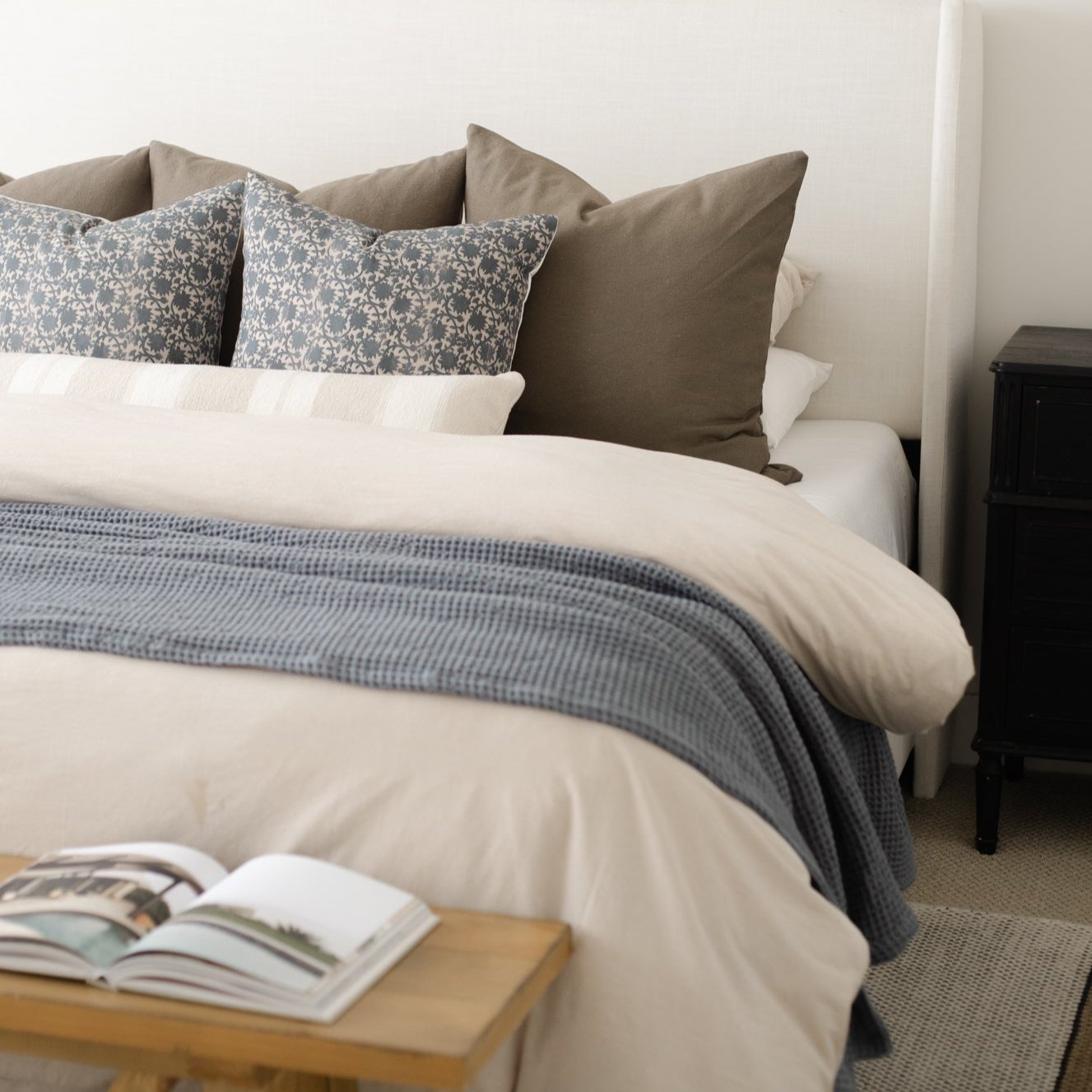 Beige duvet cover on king bed with patterned and solid pillows and blue throw blanket.