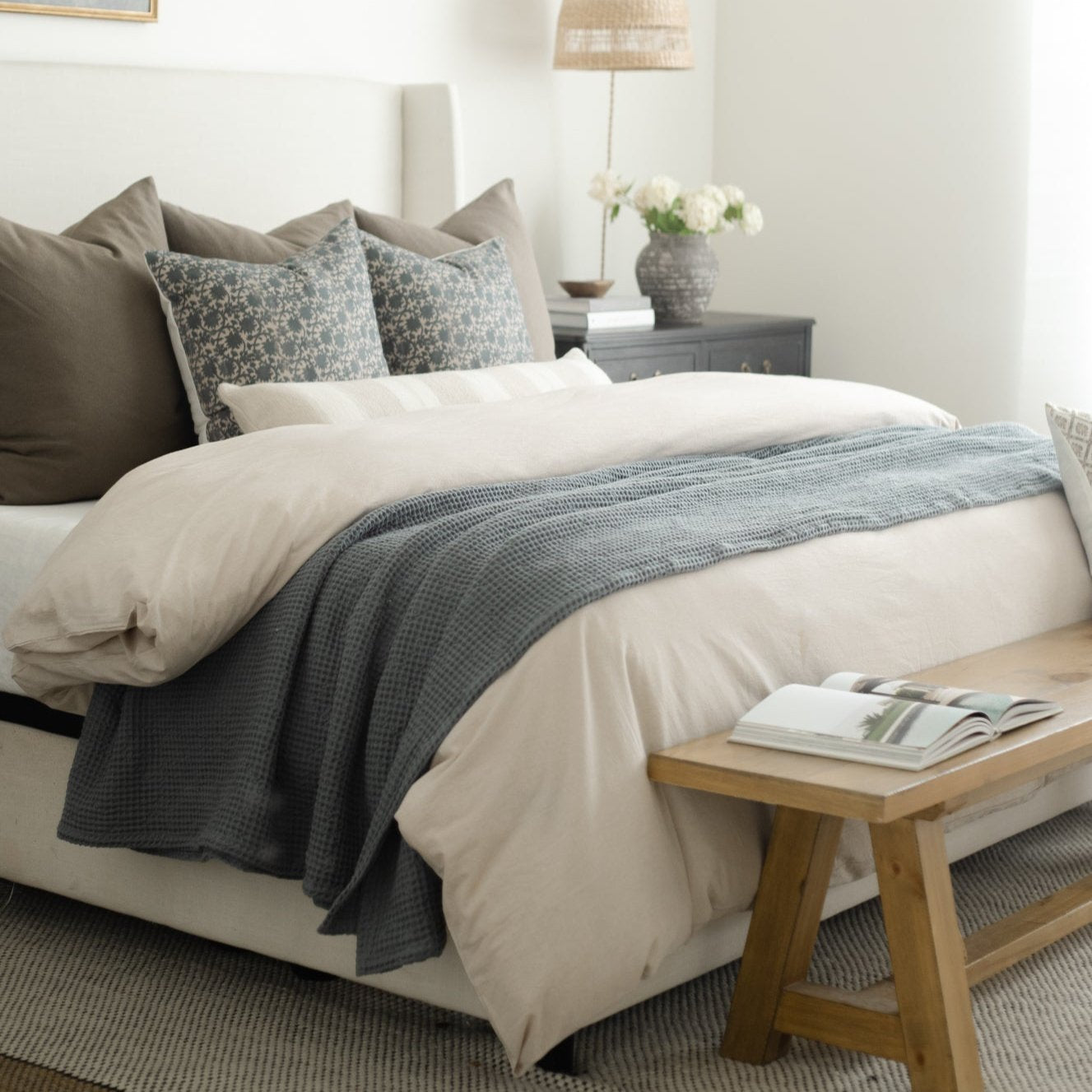 Beige duvet cover with white sheets, decorative pillows, and gray textured throw on a bed.