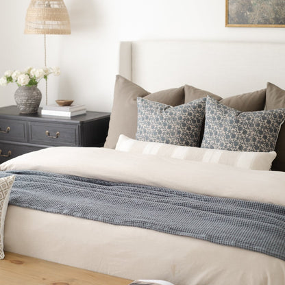 Beige duvet cover set on king bed with matching pillowcases and blue patterned throw blanket.