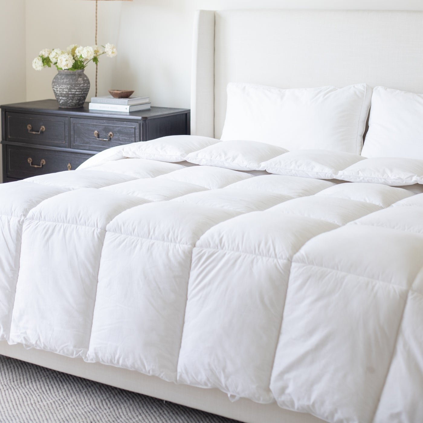 White quilted duvet insert on king bed with white pillows and upholstered headboard.