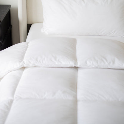 White quilted duvet insert on bed with two pillows and dark nightstand visible.