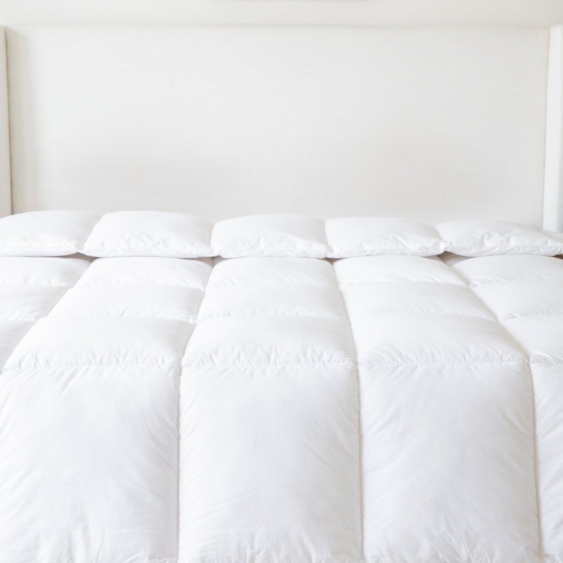 White quilted duvet insert with pillows arranged on a bed against a cream headboard.