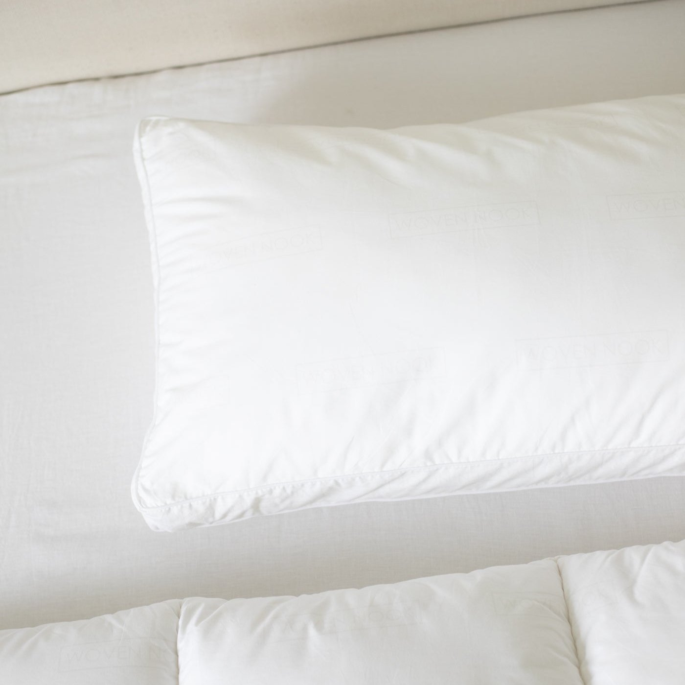 White faux down pillow insert with rounded edges resting on cream bedding.