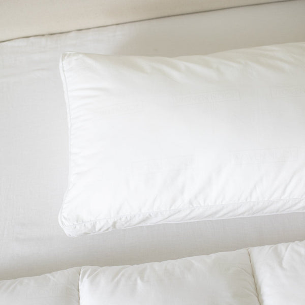 White faux down pillow insert with rounded edges resting on cream bedding.