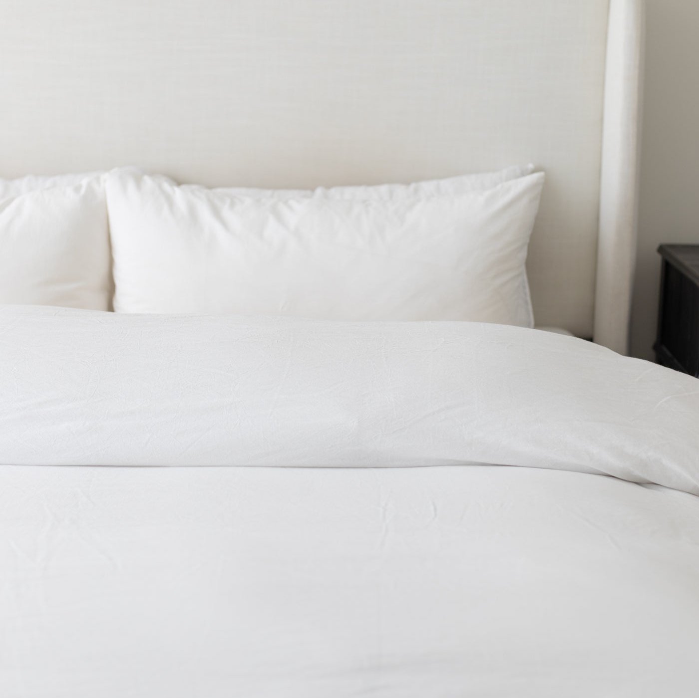 White duvet cover and pillowcases on a made bed against a neutral wall.