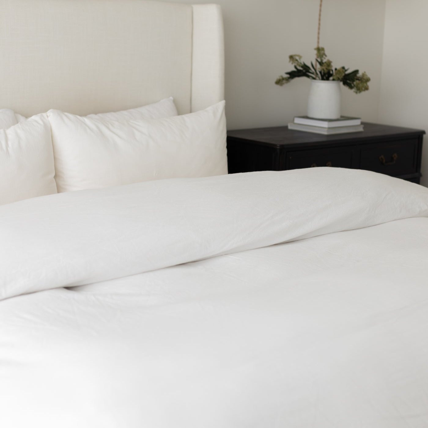 White duvet cover and pillowcases on a king-size bed with white headboard and black nightstand.