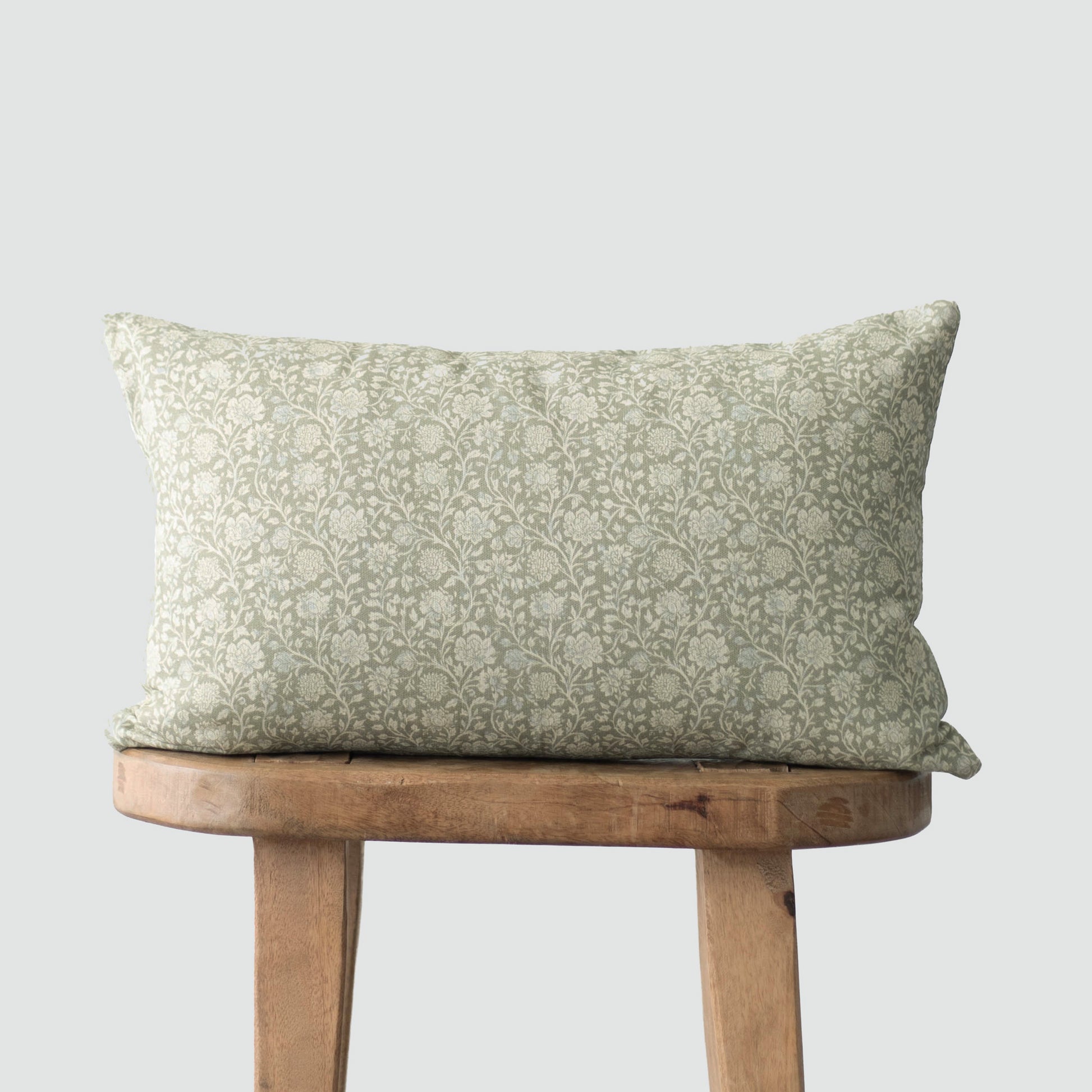 Rectangular pillow with sage green damask pattern on cream background, displayed on wooden stool.