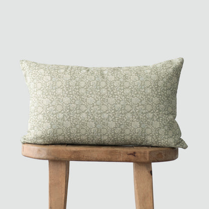 Rectangular pillow with sage green damask pattern on cream background, displayed on wooden stool.