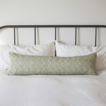 Green floral patterned lumbar pillow on white bedding with metal headboard.