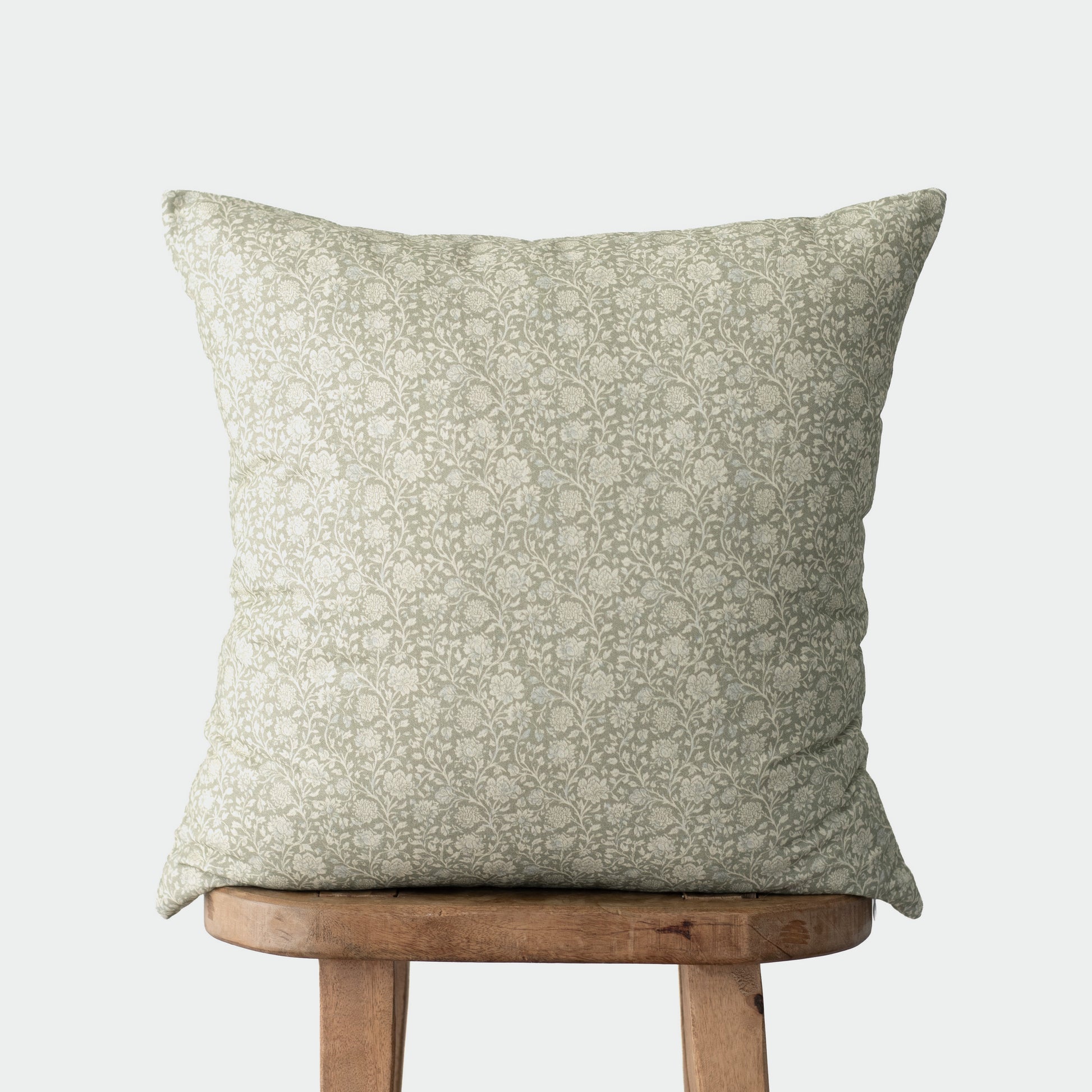 Sage green decorative pillow with damask pattern on wooden stool.