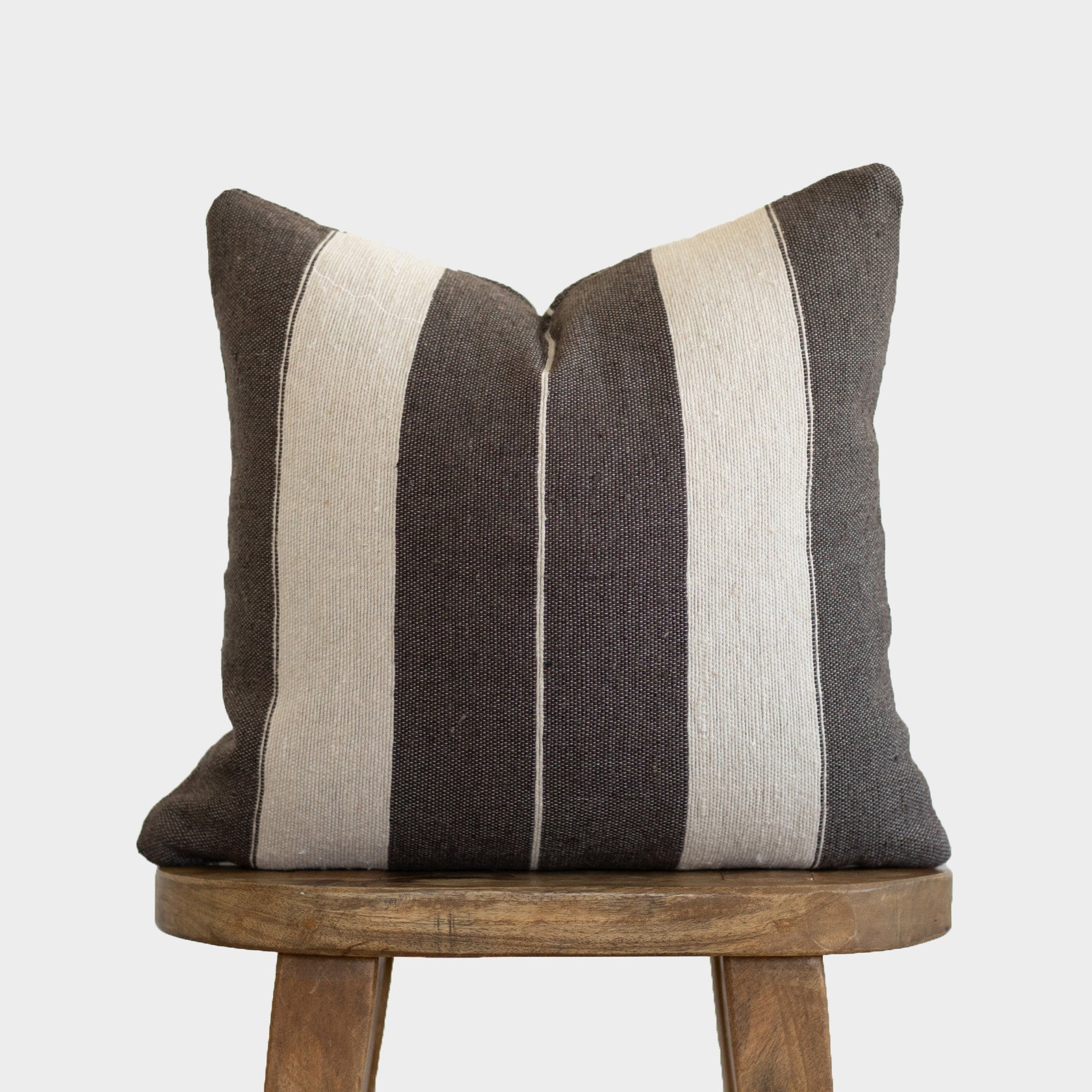 Striped pillow in charcoal and cream with vertical bands, displayed on a wooden stool.