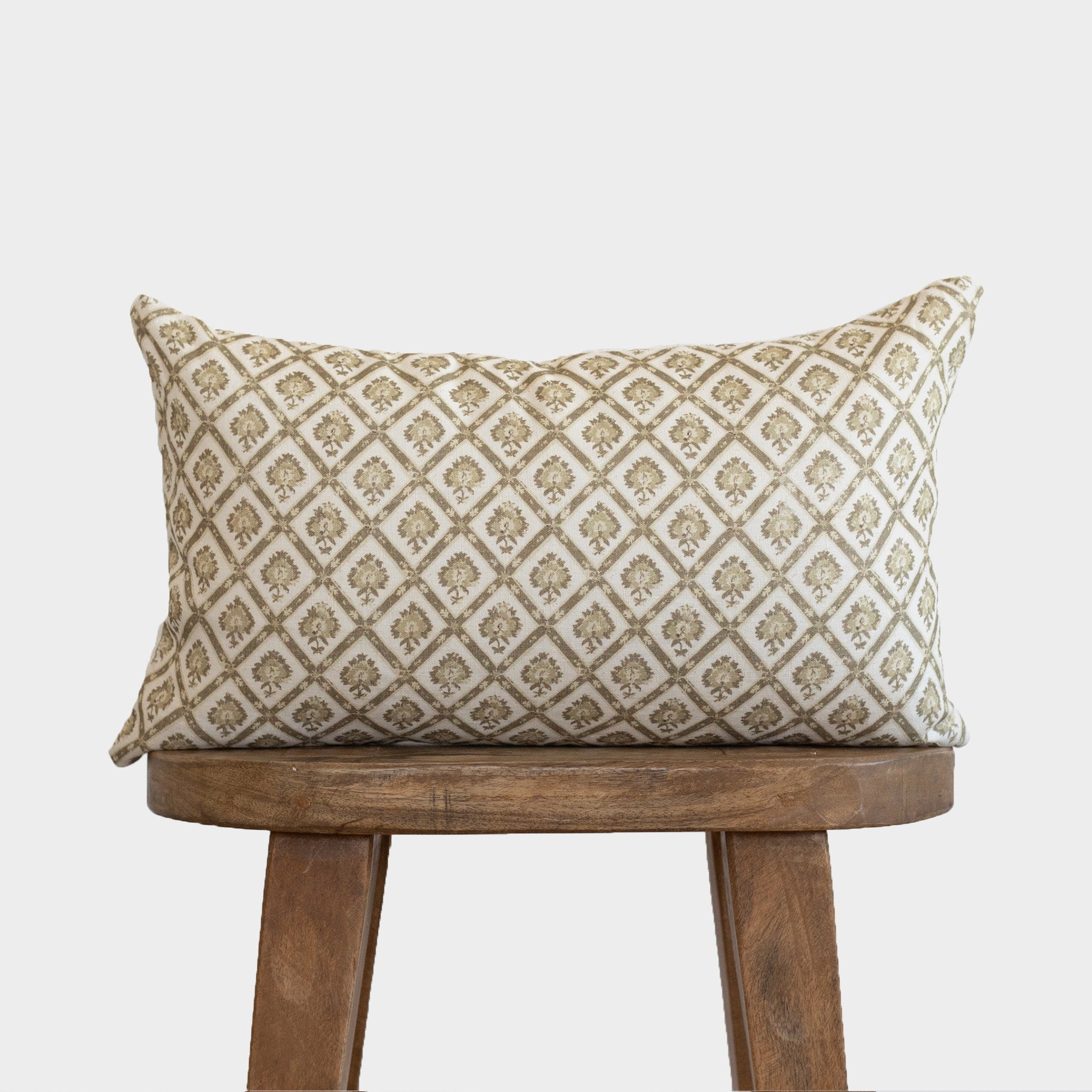 Rectangular lumbar pillow with cream linen and tan geometric diamond pattern, displayed on wooden stool.