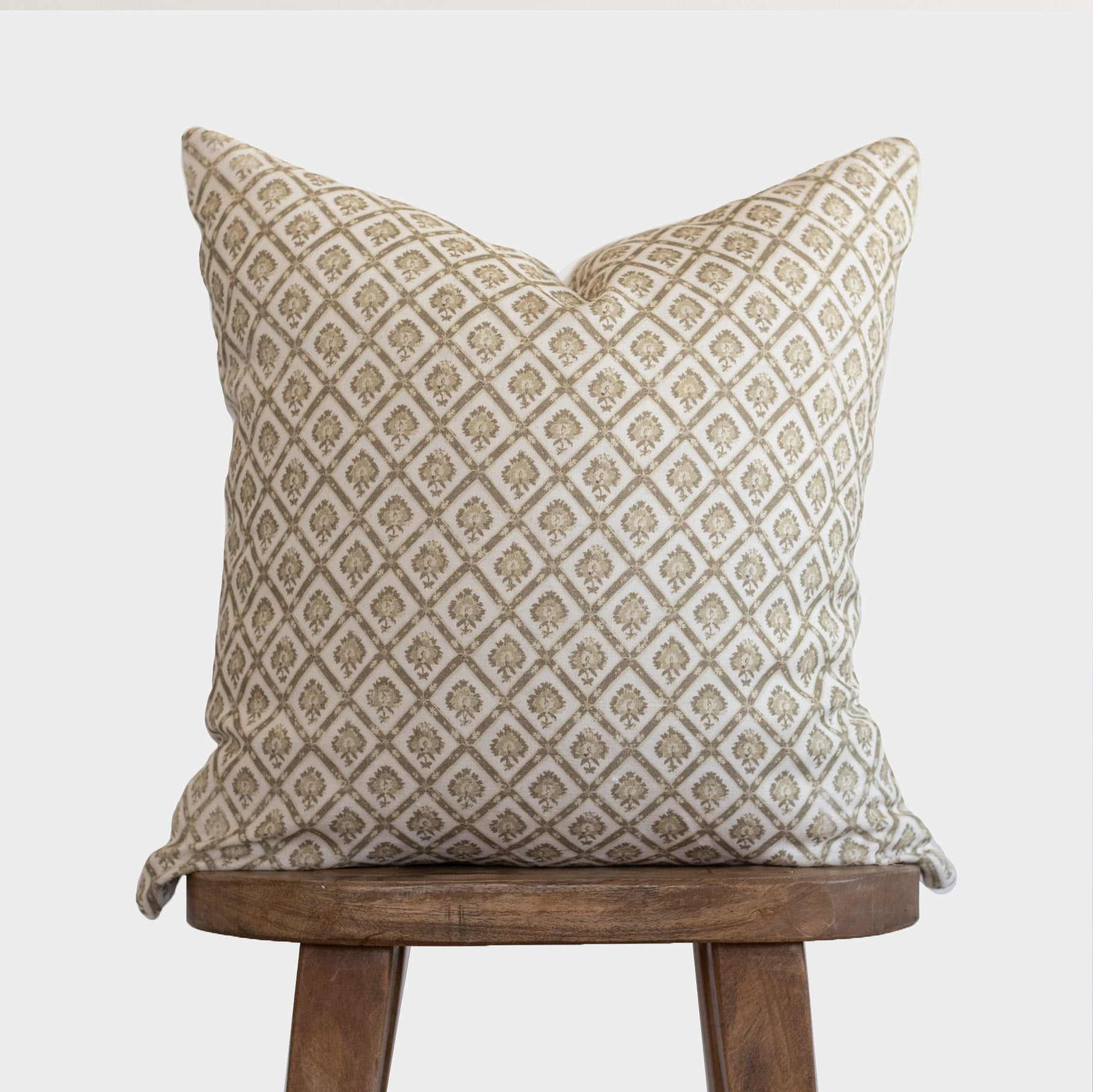 Cream linen pillow with tan geometric diamond pattern, displayed on wooden stool.